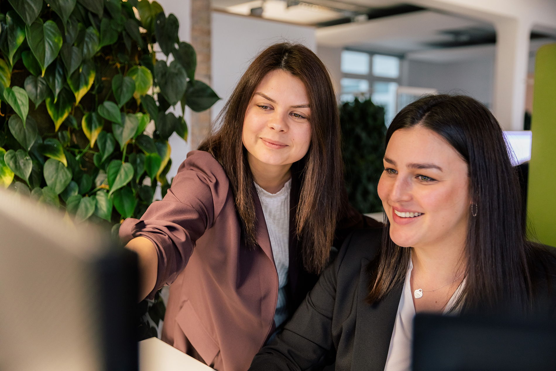 Ihre TYPO3-Agentur – Expertenmeeting bei ECONSOR zur Webentwicklung Zwei Frauen arbeiten an einem modernen Bürotisch, umgeben von üppigen Grünpflanzen, konzentriert auf einen Computerbildschirm.