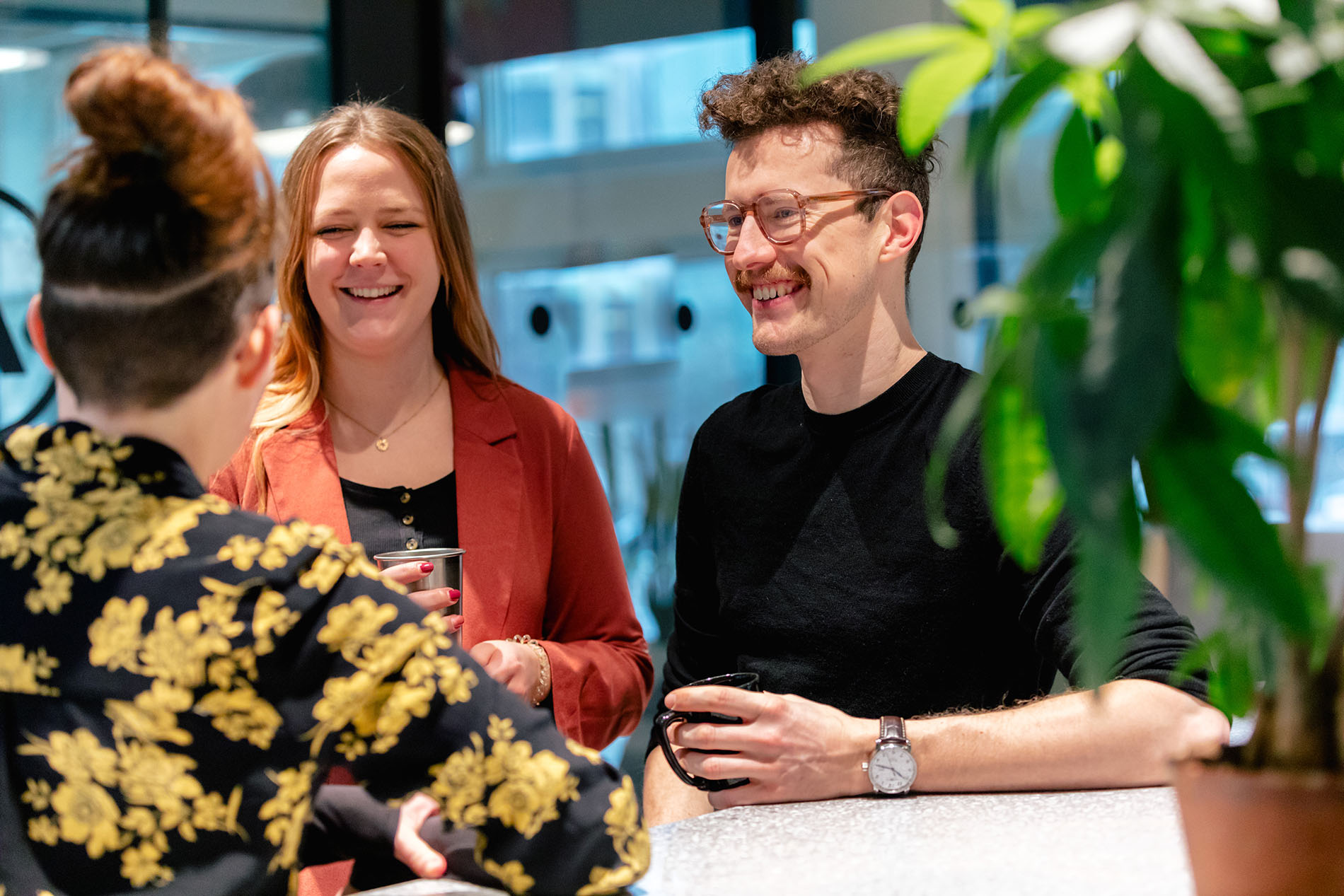 Ihre TYPO3-Agentur – Expertenmeeting bei ECONSOR zur Beratung Eine stilvoll gekleidete Gruppe von Menschen unterhält sich, mit Getränken in der Hand und Grünzeug im Hintergrund.