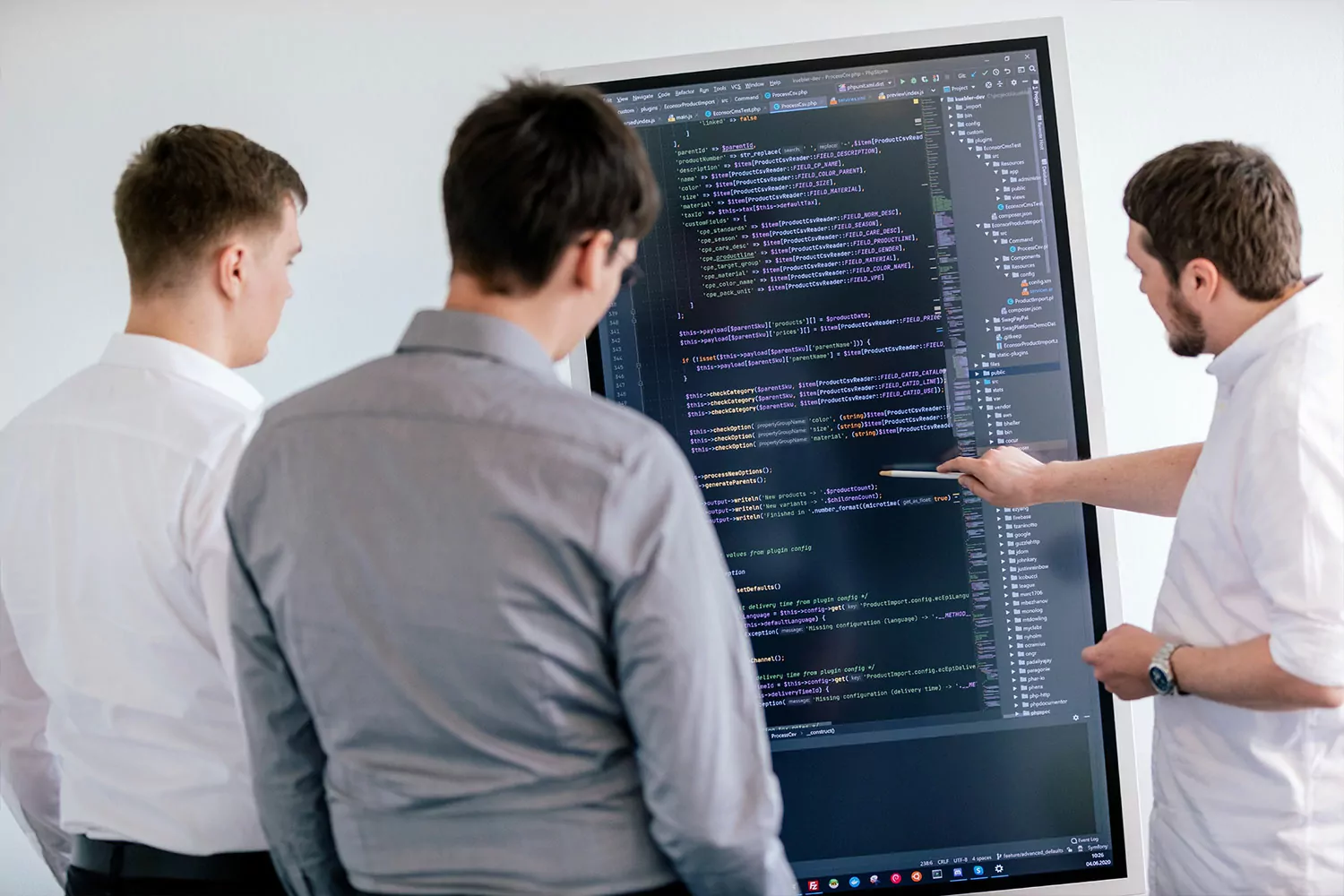 TYPO3-Entwicklung in Aktion – Experten bei der Arbeit Drei Programmierer besprechen sich vor einem großen Bildschirm mit Quellcode zur Entwicklung einer TYPO3-Erweiterung.