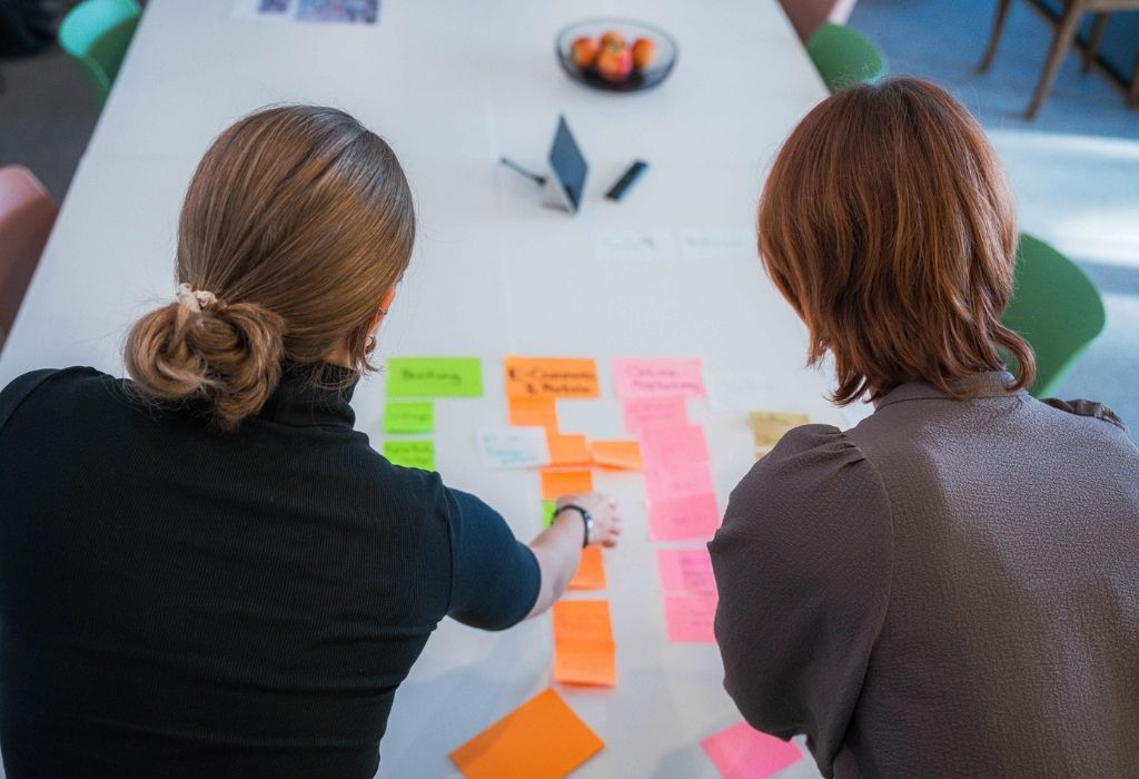 Zwei Personen planen ein Projekt mit farbigen Post-its auf einem Tisch.