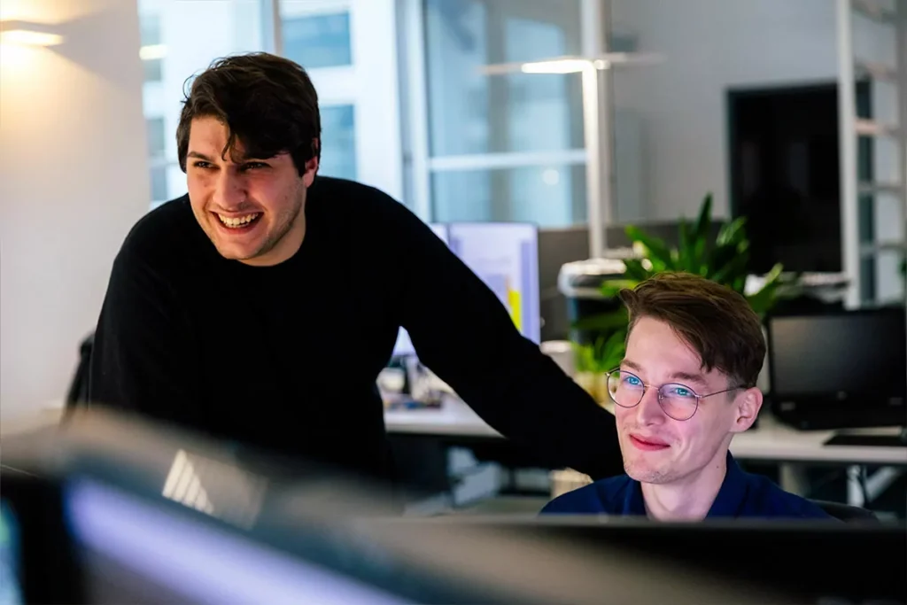 Ihre TYPO3-Agentur für Updates Ein Mitarbeiter unterstützt einen Kollegen bei der Wartung und Aktualisierung einer TYPO3-Website an mehreren Bildschirmen.