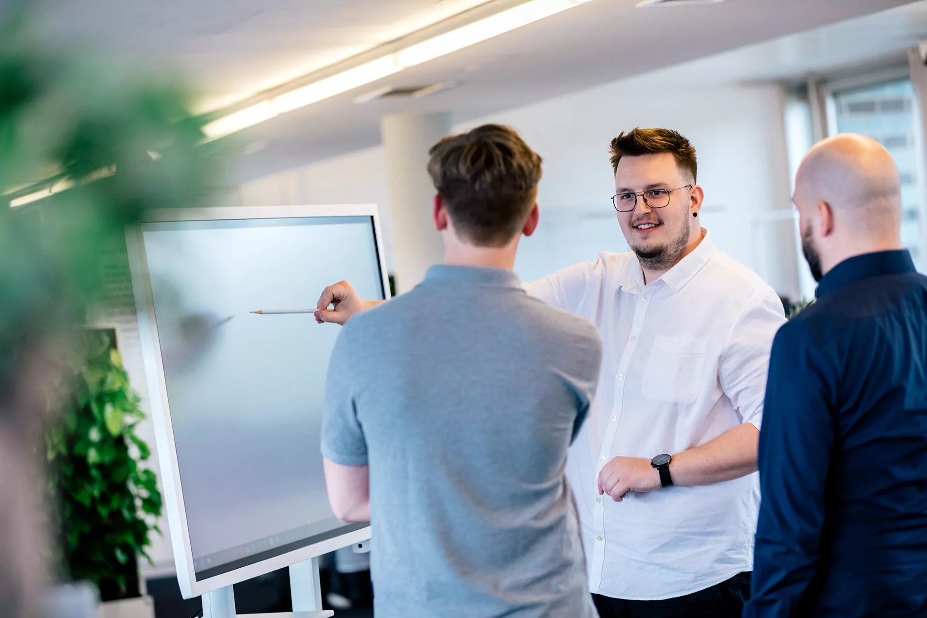 Ihre TYPO3-Agentur in Stuttgart – Expertenmeeting bei ECONSOR zur Webentwicklung Drei Fachleute führen in einem modernen Büro eine Diskussion, wobei einer mit einem Stift auf einen Bildschirm zeigt.