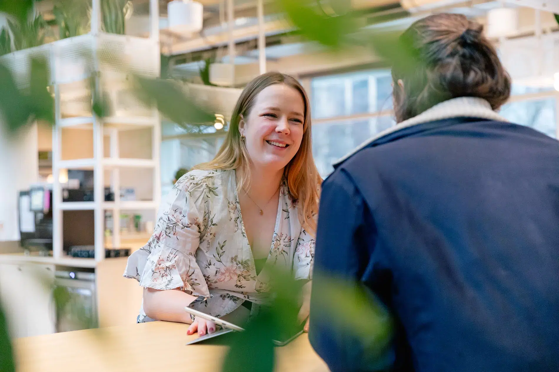 Ihre TYPO3-Agentur – Expertenmeeting bei ECONSOR in Karlsruhe Zwei Personen unterhalten sich an einem Holztisch in einem modernen, mit Pflanzen gefüllten Arbeitsraum. Einer hält ein Tablet in der Hand.