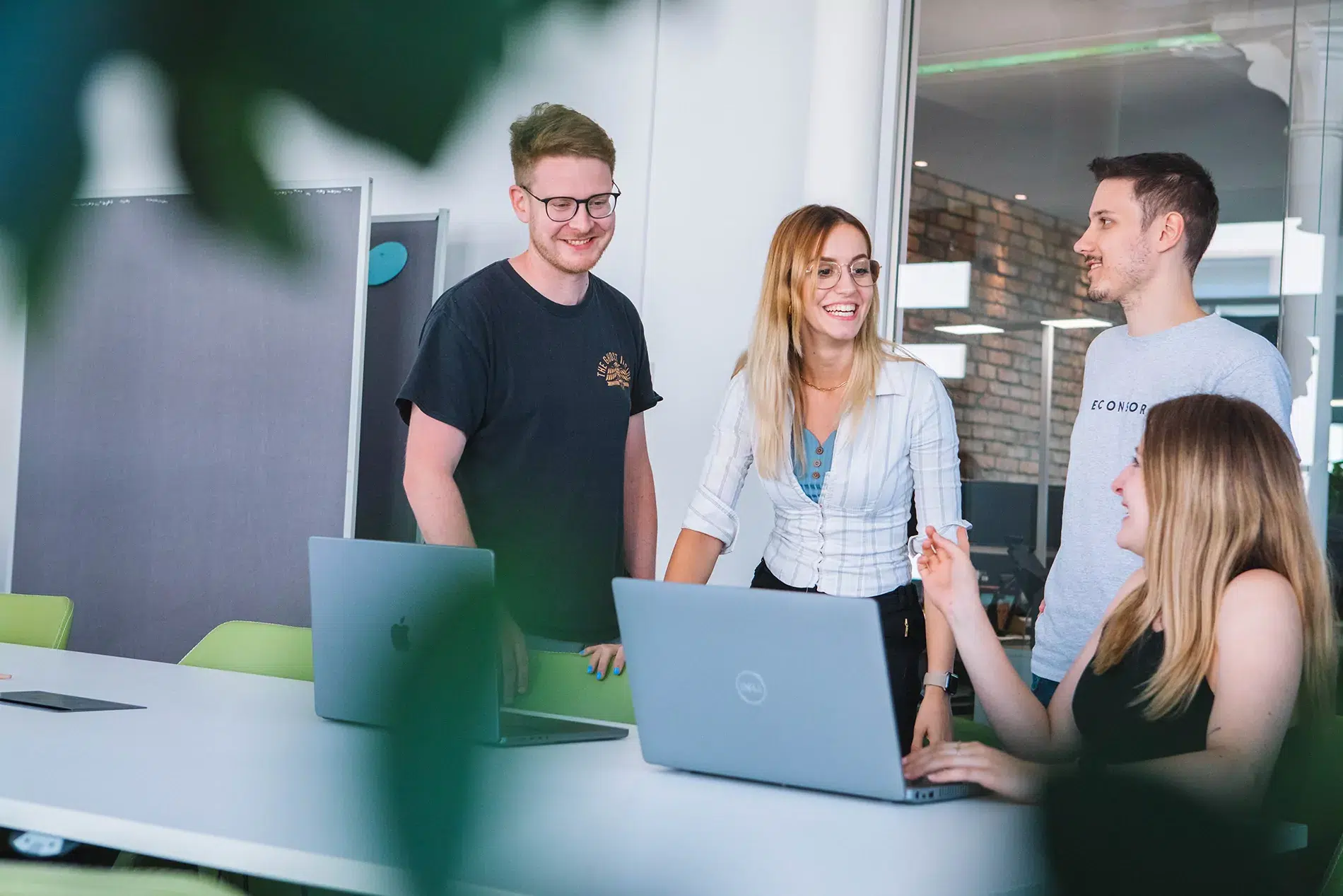 Eine Gruppe von vier Geschäftsleuten, die in einem hellen, modernen Büro mit Laptops zusammenarbeiten und diskutieren.